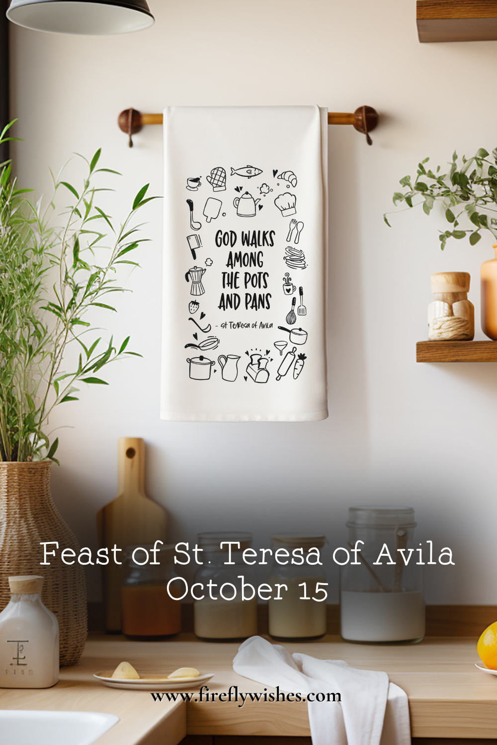 Kitchen towel printed with the quote “God walks among the pots and pans” by St. Teresa of Avila, hanging in a warm, light-filled kitchen with greenery and wooden accents.