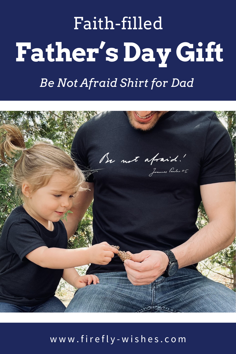 Dad wearing a “Be Not Afraid” shirt sits with his young daughter, sharing a pinecone and smiling.