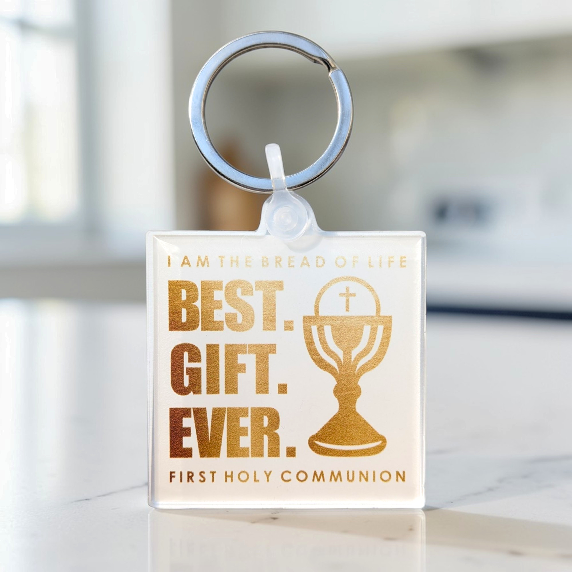 Keychain with 'Best Gift Ever' and First Holy Communion text on a blurred background
