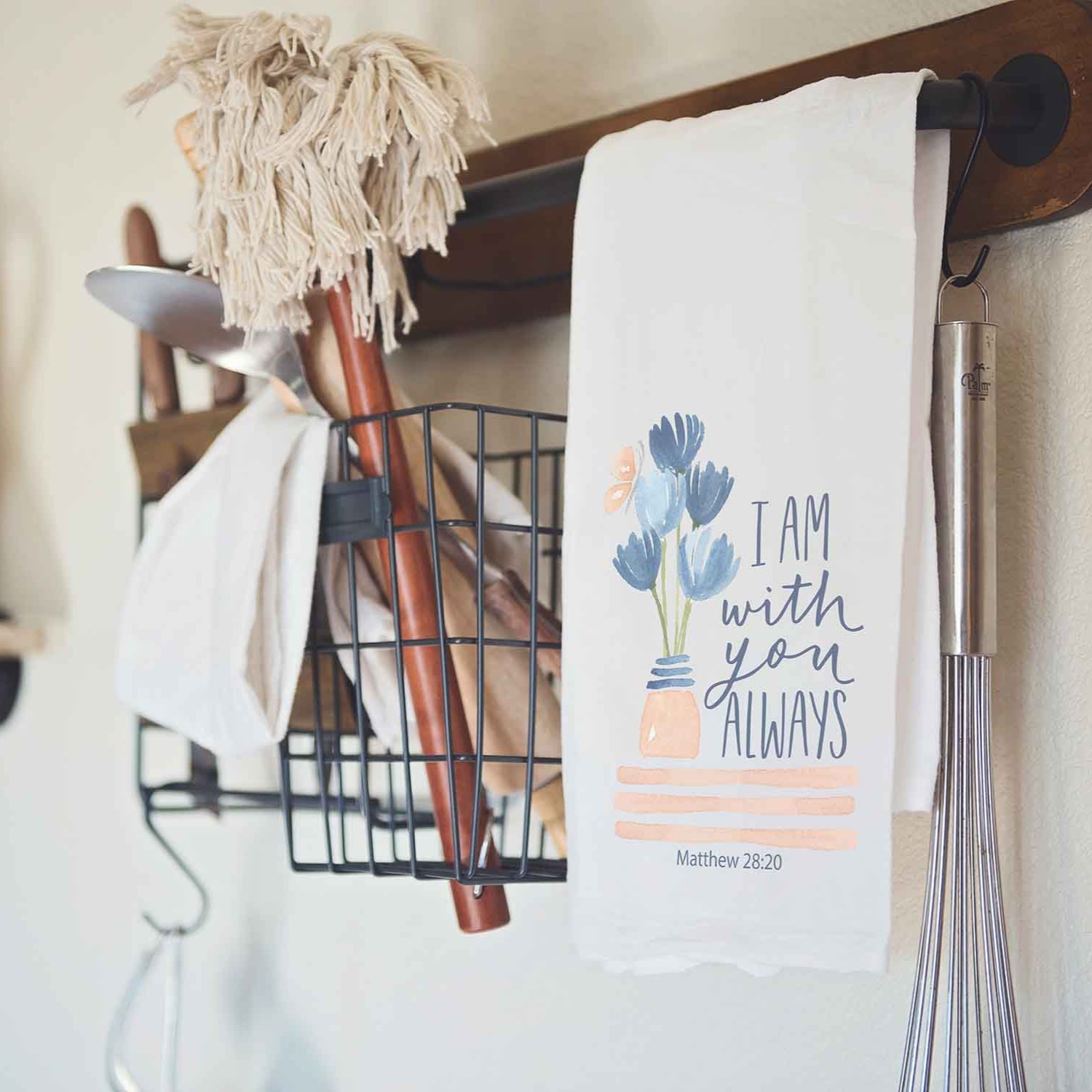 Christian kitchen towel with 'I am with you always' text hanging on a rack with cleaning supplies.