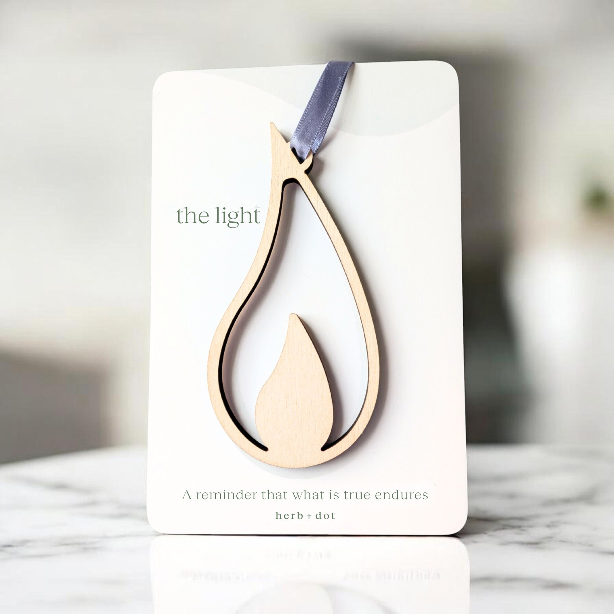 Decorative wooden pendant on a card with 'the light' text, displayed on a marble surface.