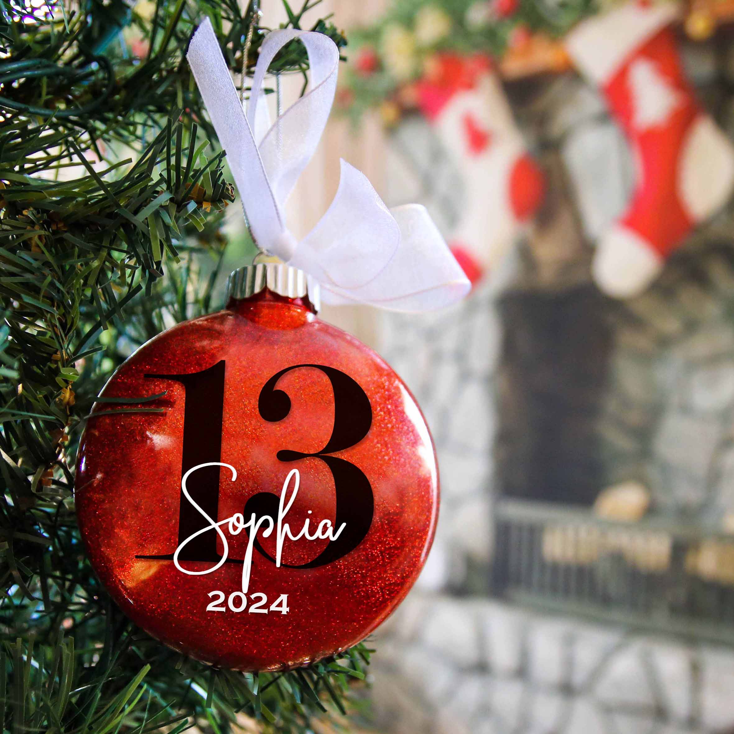 Red glittered ornament with the number 13 and Sophia 2024 hanging in a Christmas tree