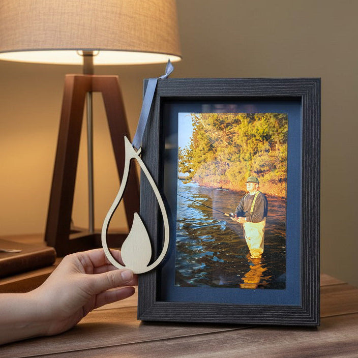 Framed photograph of a person fishing on a lake with a decorative flame ornament and lamp in the background.